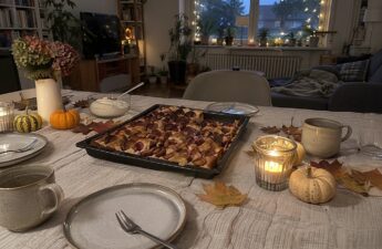 Geburtstagstisch mit Zwetschgenkuchen, Windlichtern, Zierkürbissen und Herbstlaub im warmen Abendlicht